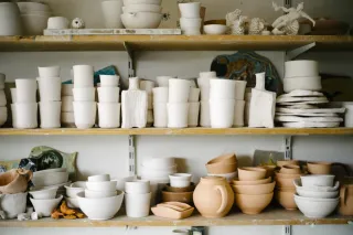 Rows of ceramic bowls, cups, plates and unfinished pottery fill workshop shelves.