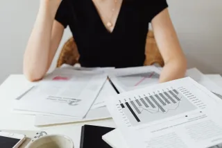 A printed report with a bar-and-line chart is held above other financial papers on a desk.